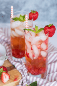 pink drink in glass with ice and topped with strawberries on side of glass
