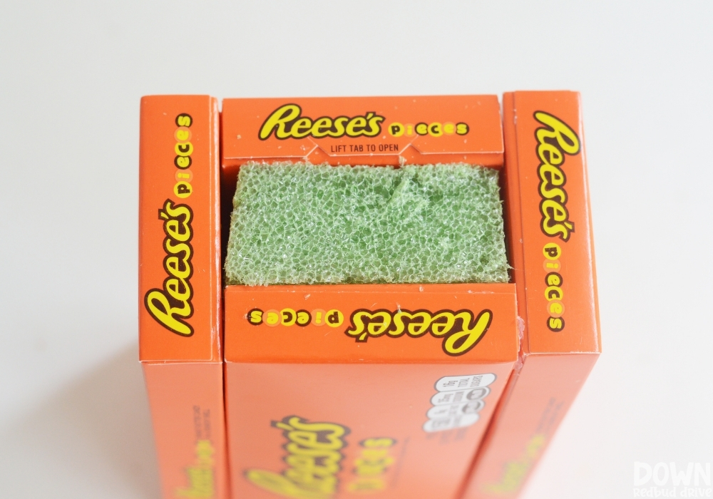 A piece of floral foam pressed in-between 4 boxes of Reese's Pieces for the DIY Reese's Bouquet.