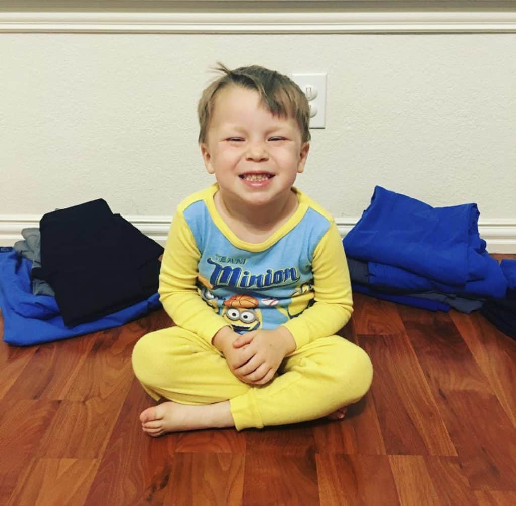 A toddler boy sitting proudly in front of clothes that he folded himself. 