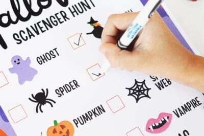 Kid's hand using a marker to mark off items on a halloween checklist.