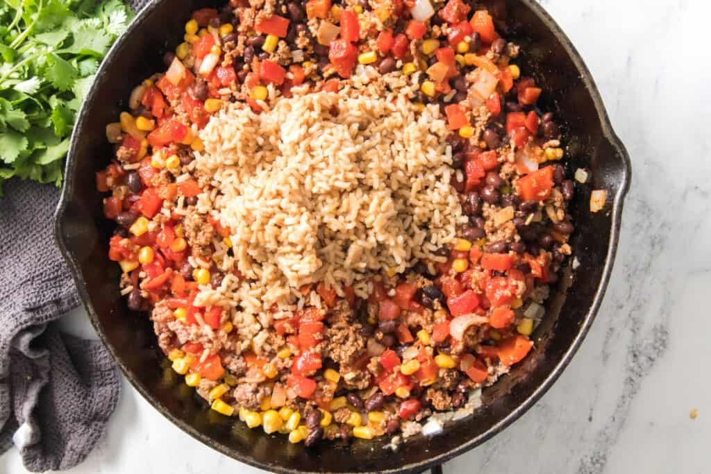 brown rice added with ingredients in cast iron skillet for ground beef and beans recipe