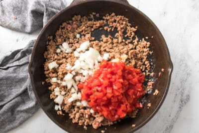 Ground beef, tomatoes, and onions in a cast iron skillet