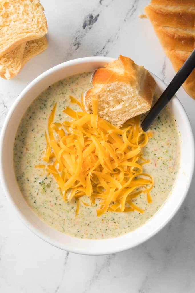 overhead shot of broccoli cheese soup in bowl with cheese and bread