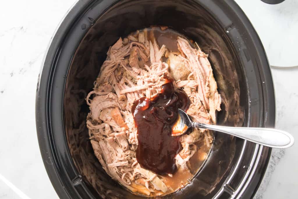 shredded pulled pork in slow cooker with bbq sauce and spoon