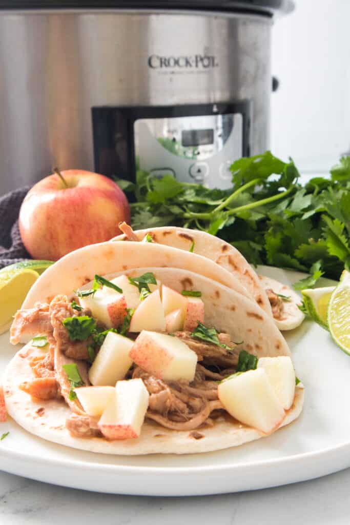 pulled pork tacos with apple slaw on plate and slow cooker in the background