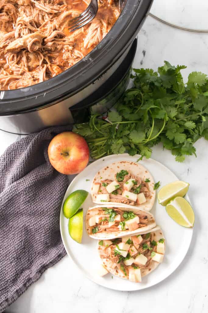 overheat shot of slow cooker pulled pork tacos plated with cilantro and lime wedges