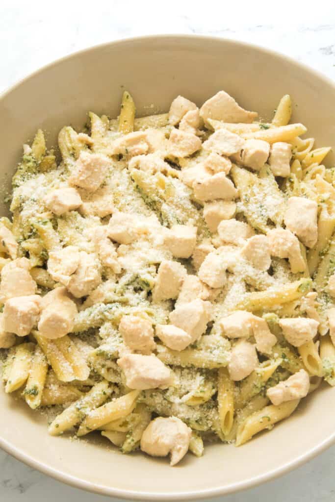 vertical shot of chicken pesto pasta in serving bowl with grated cheese