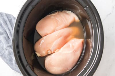 Raw chicken and broth in a slow cooker