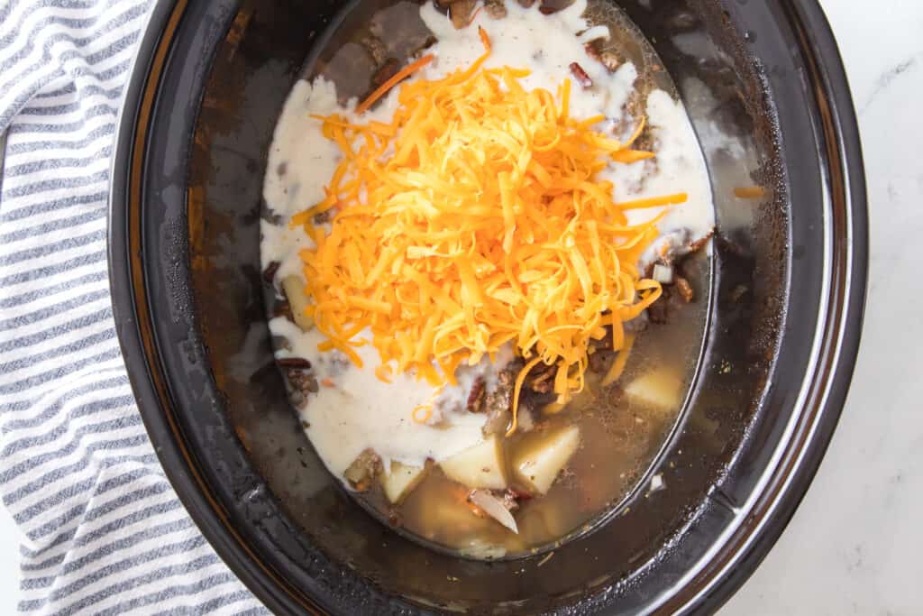 shredded cheese and roux added to slow cooker with hamburger, bacon, vegetables and chicken broth