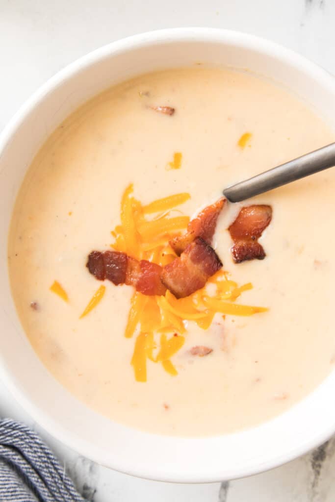 overhead close up shot of potato soup recipe in white bowl topped with cheese and bacon