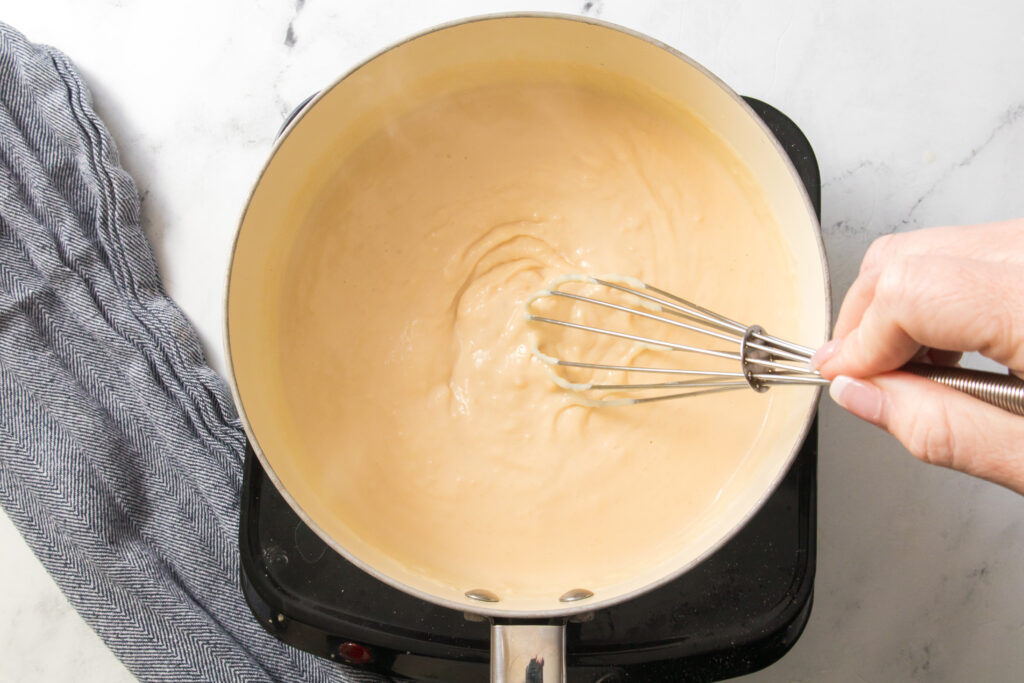 hand stirring melted butter and flour with whisk in a saucepan to make a roux