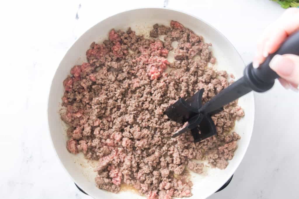 large skillet browning ground beef breaking meat up with a mix n chop