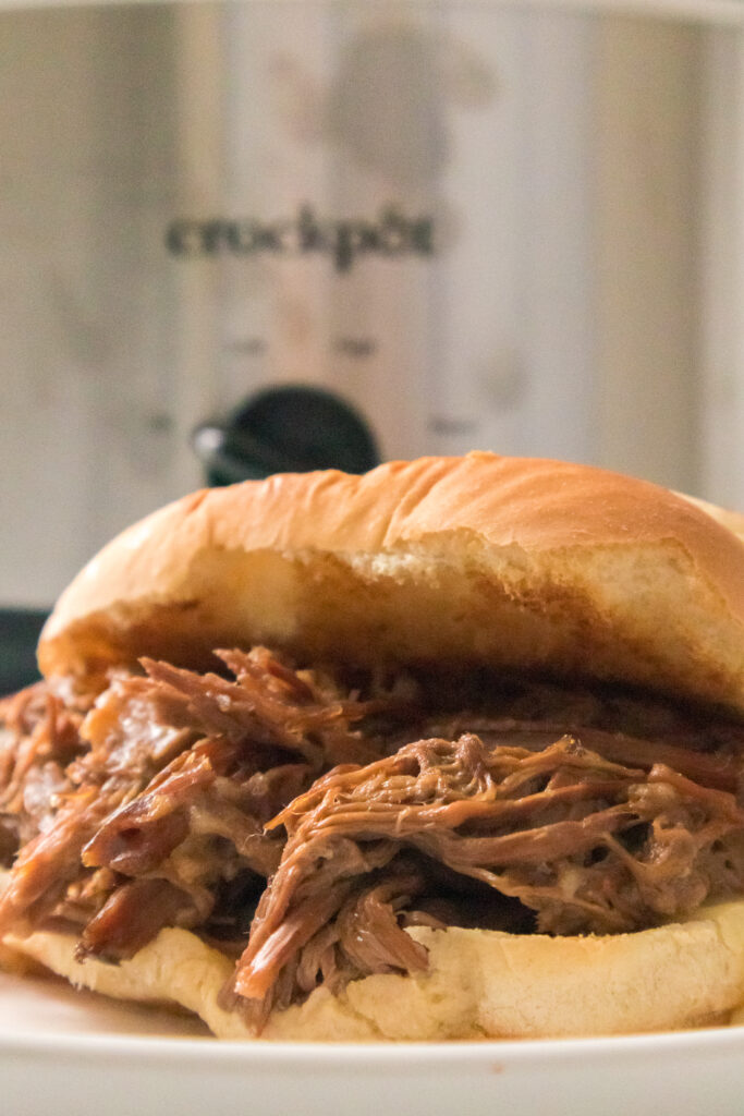 close up shot of french dip sandwich with slow cooker in the background