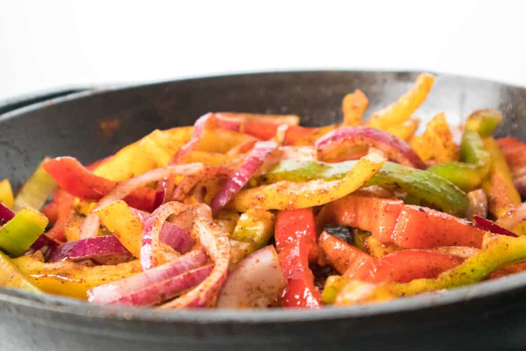 bell peppers and red onion cooking with fajita mix in cast iron skillet