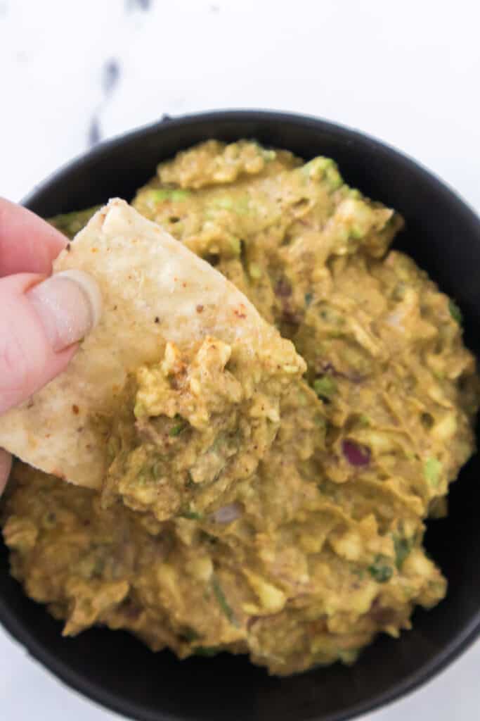 hand dipping chip into guacamole salsa