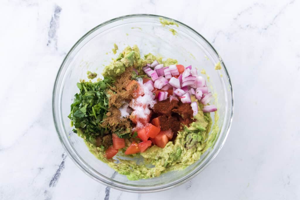 avocados, red onion, tomatoes, cilantro, salt, cumin and chili powder in glass bowl