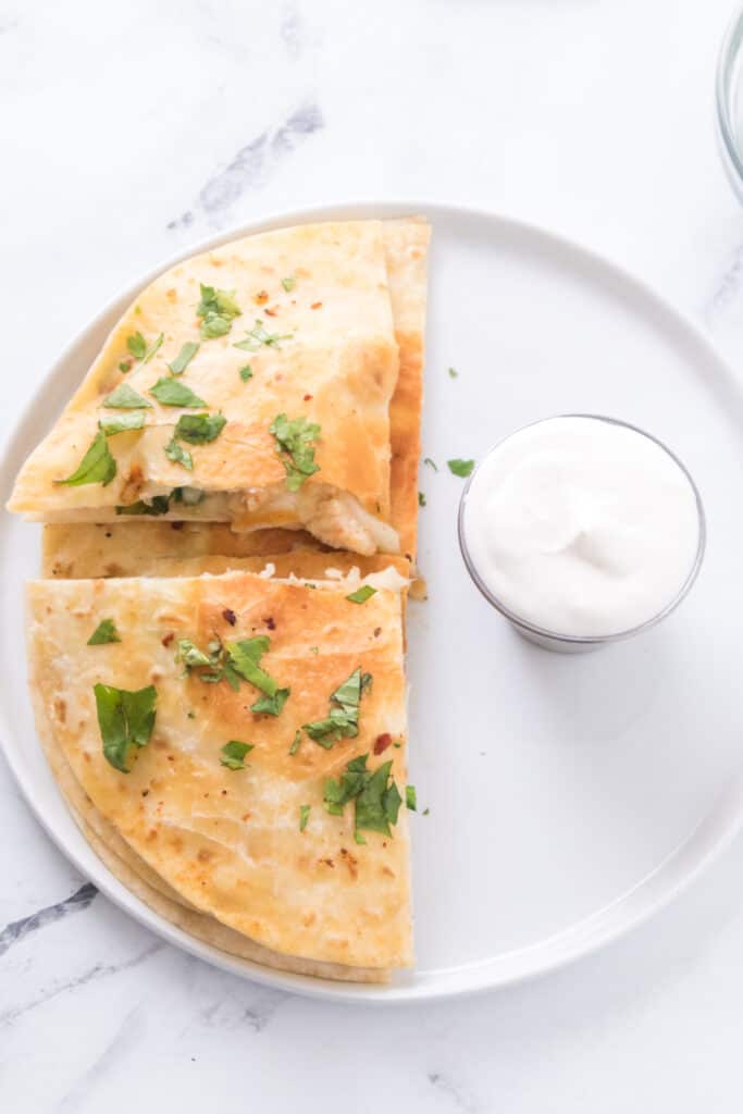 chicken and spinach quesadilla on white plate with chopped cilantro and sour cream