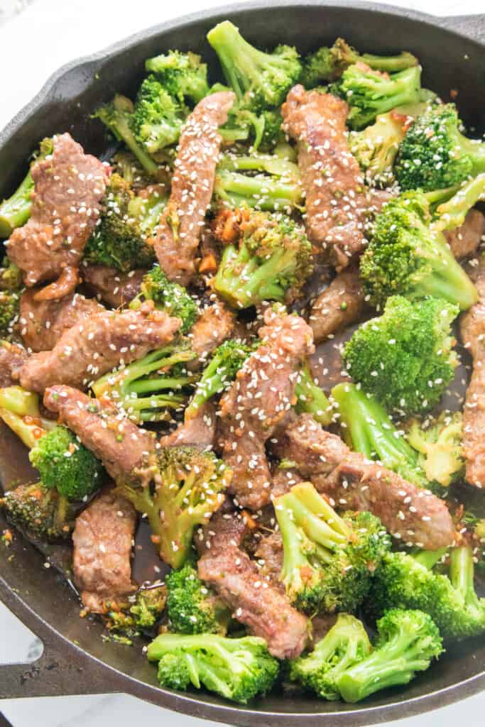 vertical close up of beef and broccoli stir fry topped with white sesame seeds