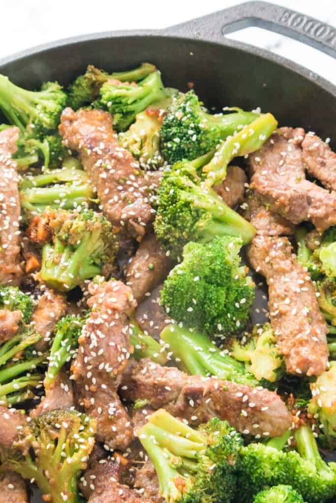 close up of beef and broccoli recipe cooked in cast iron pan topped with sesame seeds