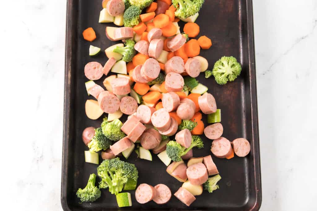broccoli, zucchini, carrots, red potatoes and sliced chicken apple sausage on baking sheet 