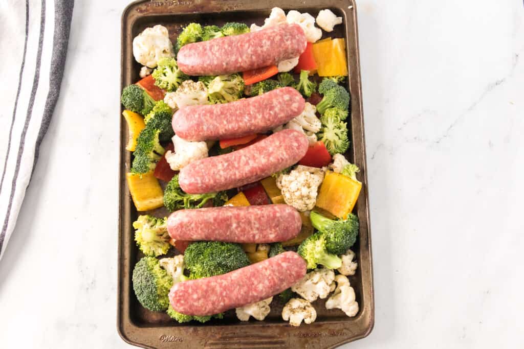 Italian sausage on top of raw vegetables on baking sheet