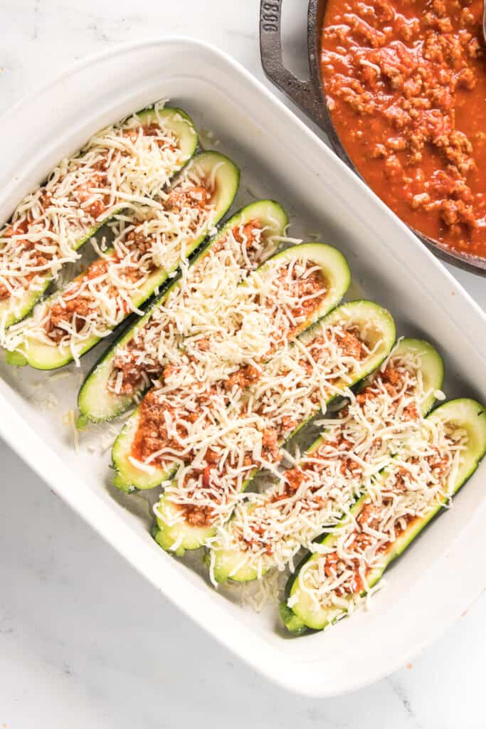overhead shot of stuffed zucchini boats in baking dish  with marina in cast iron skillet