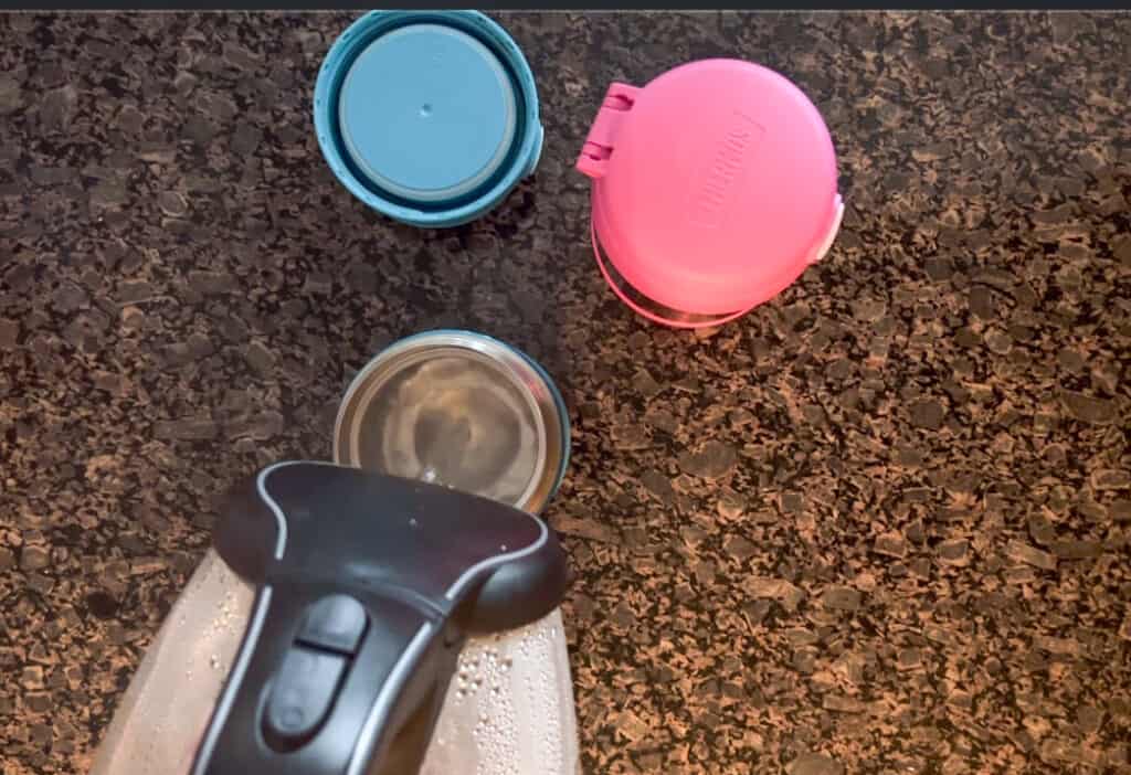 This image shows boiling water being poured from a tea kettle into a thermos funtainer food container. 