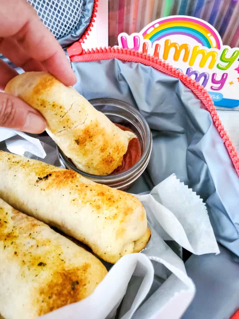 Pizza dippers in a lunch box with tomato sauce for dipping.