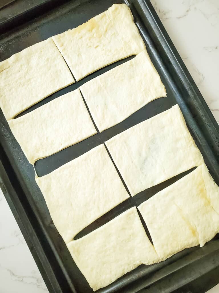 Pizza dough rolled out flat onto a baking sheet and cut into 8 rectangles.