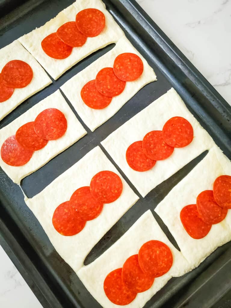 Pizza dough rectangles topped with 3 slices of pepperoni each.