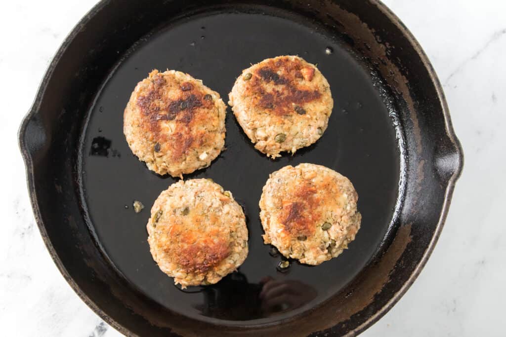 salmon cakes cooking in cast iron skillet