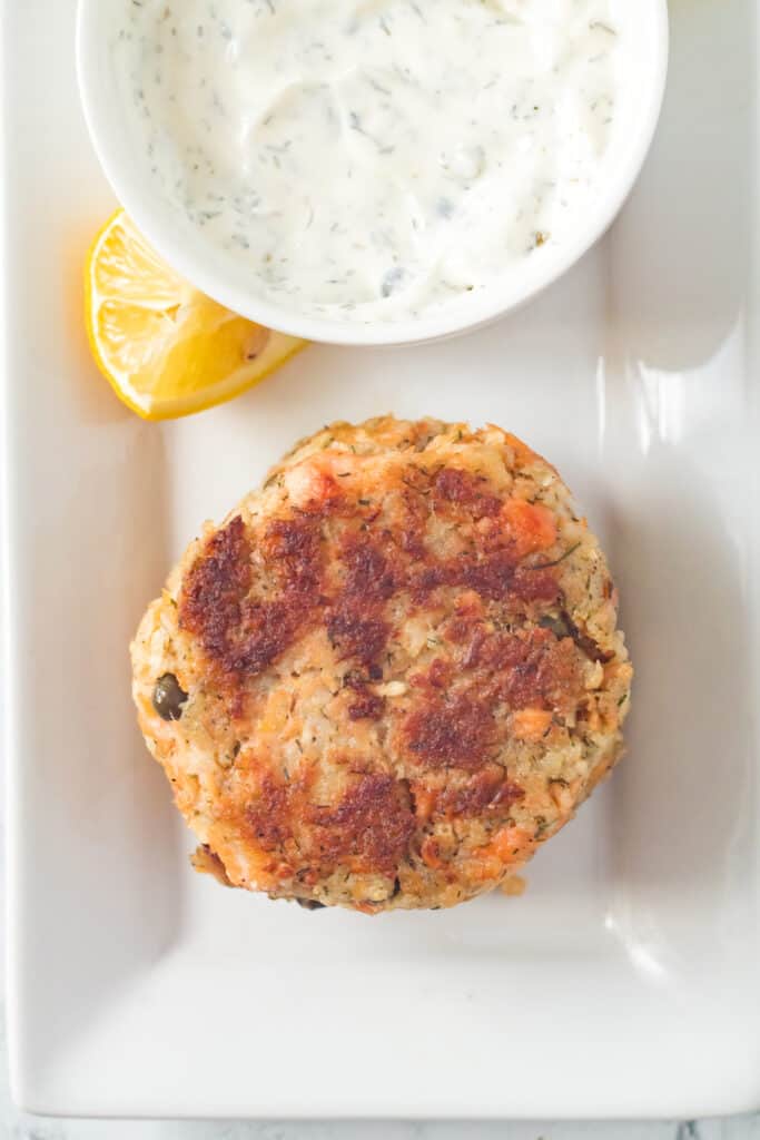overhead shot of salmon cake on serving platter with dill caper sauce and lemon