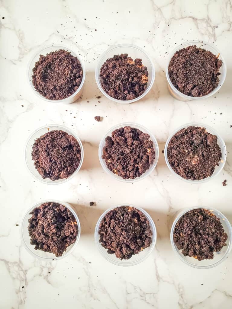 This image shows the final layer of cookie crumbles being added to the top of the pudding cups. 