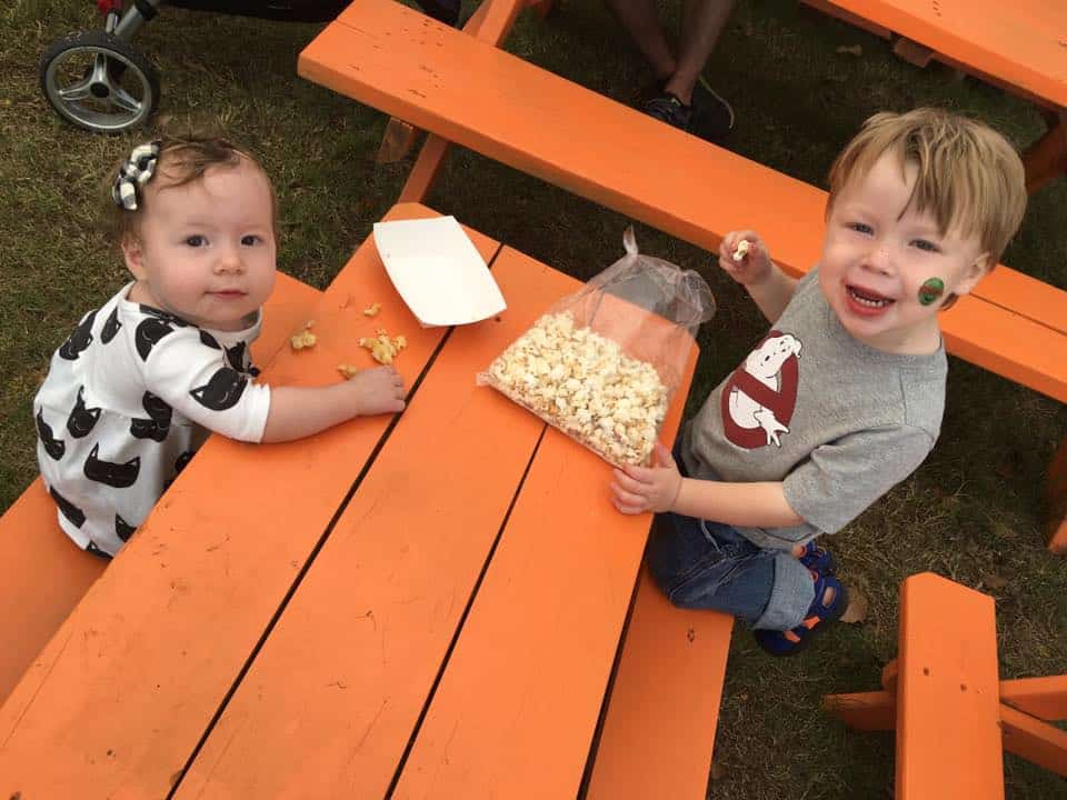 A photo of two toddlers eating kettle corn at an orange picnic table at a pumpkin patch in fort worth. 