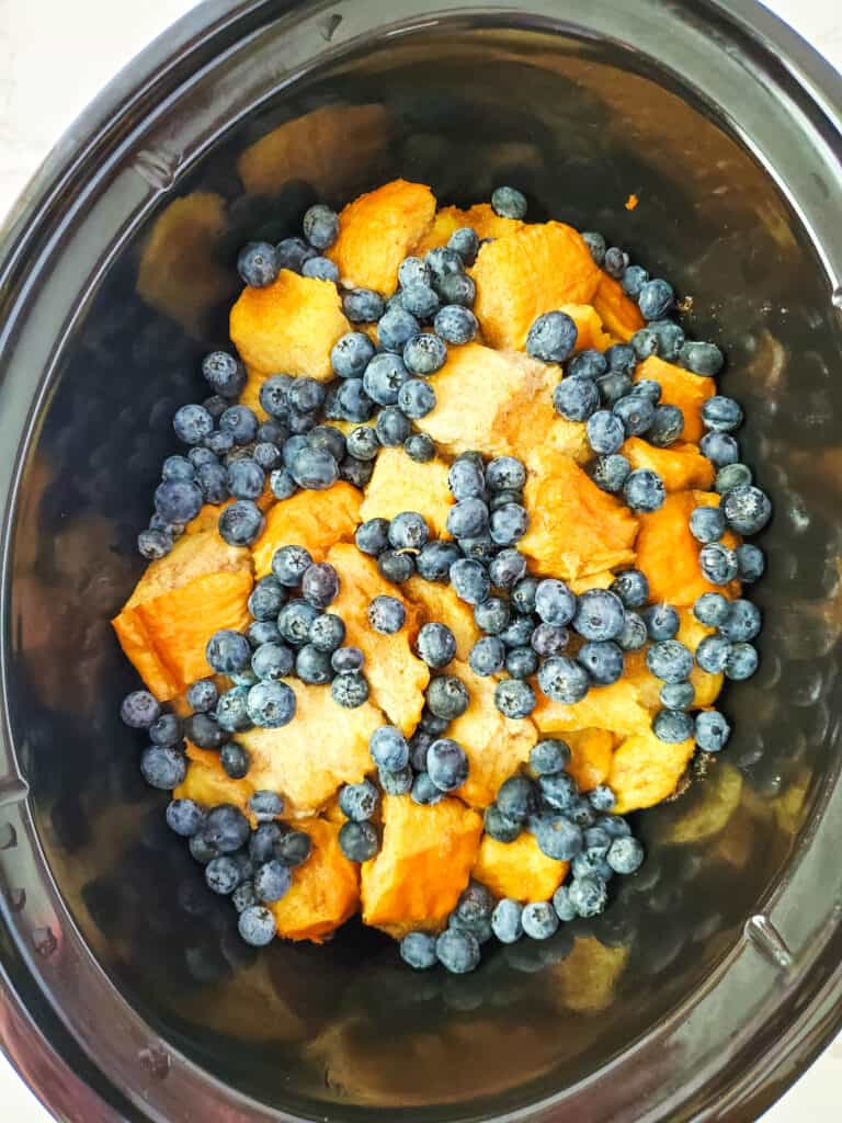 Adding blueberries to the top of the french toast casserole.