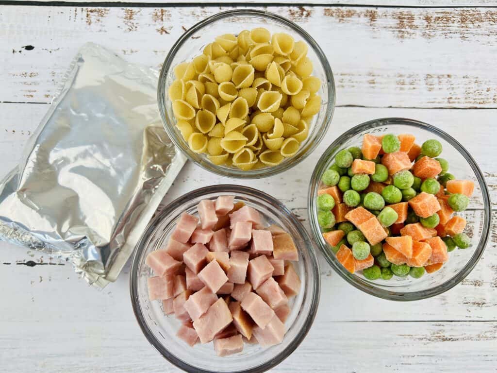 ingredients for leftover baked ham macaroni and cheese: macaroni, cheese packet, ham cubes, peas and carrots.