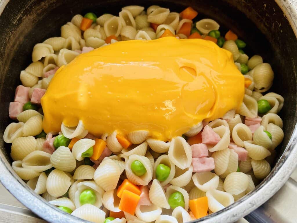 adding cheese sauce packet to macaroni noodles, ham, and peas and carrots.